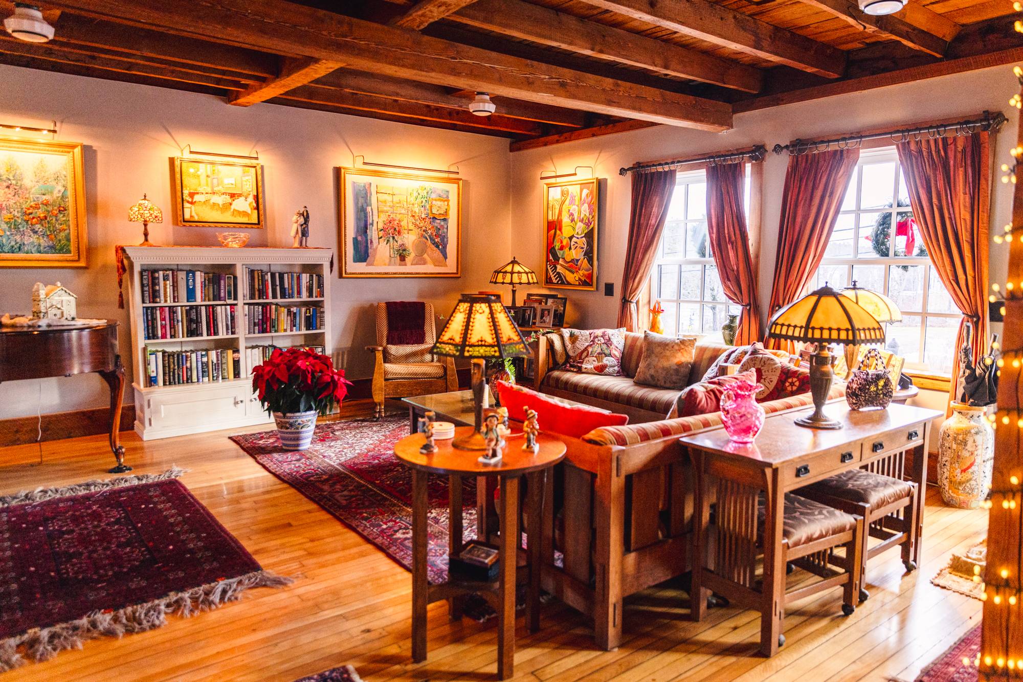 The great room of the 1850s house, with original beams, a grand piano, and warm gathering spaces