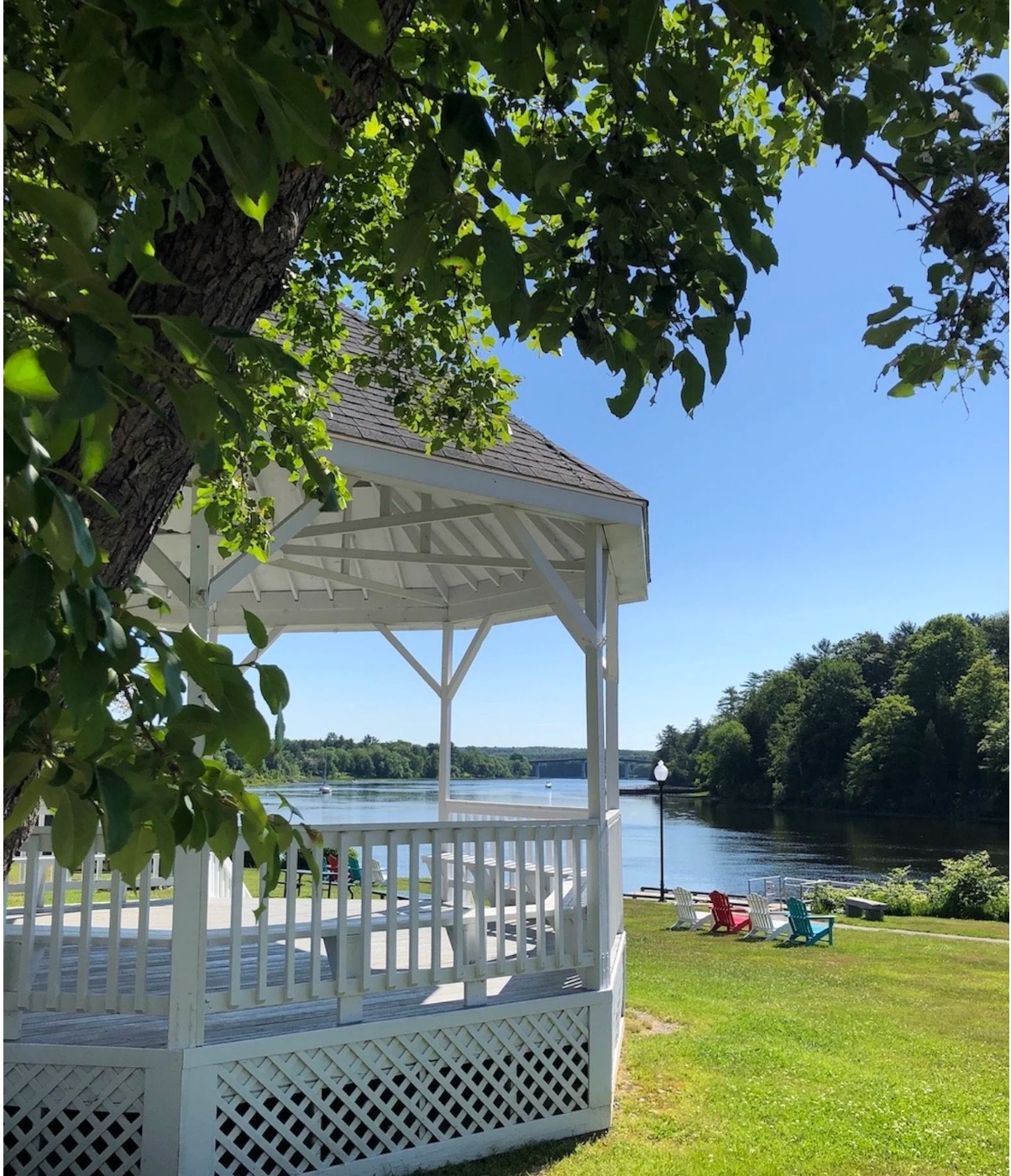 The Kennebec River at the Richmond waterfront — a white gazebo framed by summer trees, Adirondack chairs on the lawn, and the calm river beyond